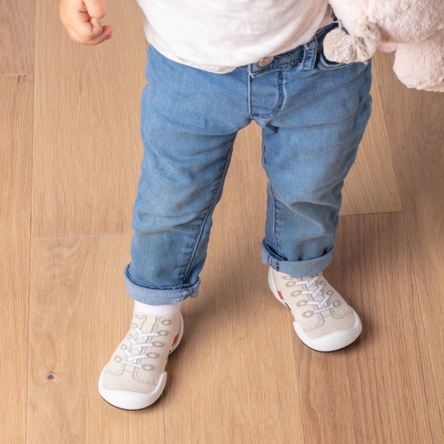 Child in jeans and sock shoes standing on wood floor.