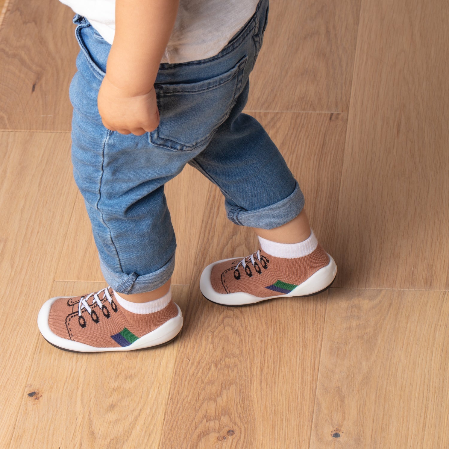 Toddler wearing blue jeans and brown sock shoes on wooden floor.
