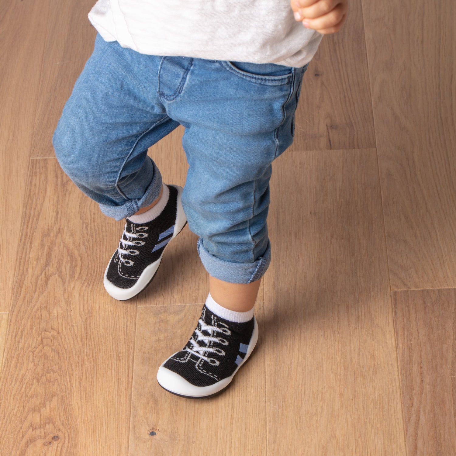 Toddler in jeans and sneaker socks on hardwood floor.