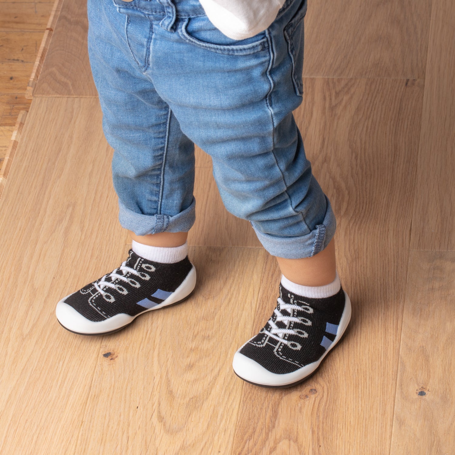Toddler in jeans and sock shoes on wooden floor.