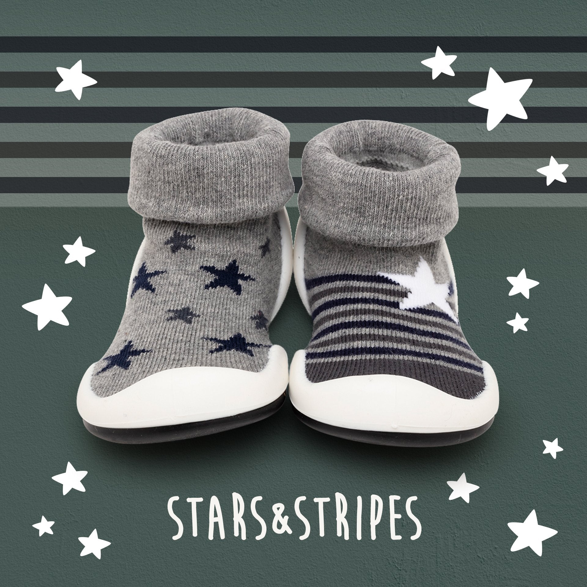 Two baby slipper-socks with white soles, gray fold-down cuffs, and star and stripe designs against a striped green backdrop with white stars and white script.