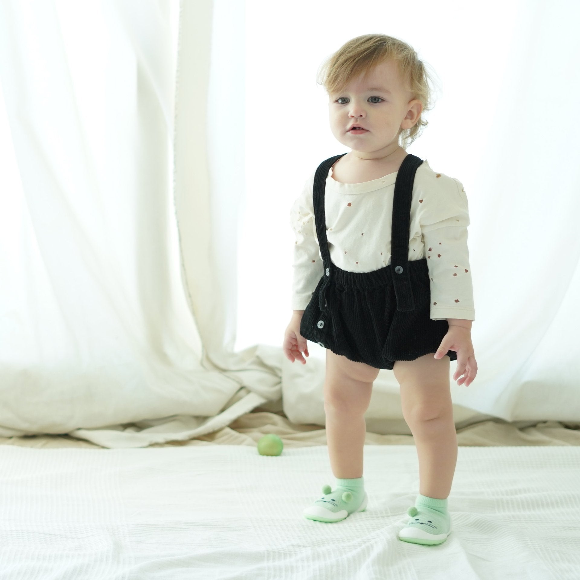 Baby in black overalls and green socks.
