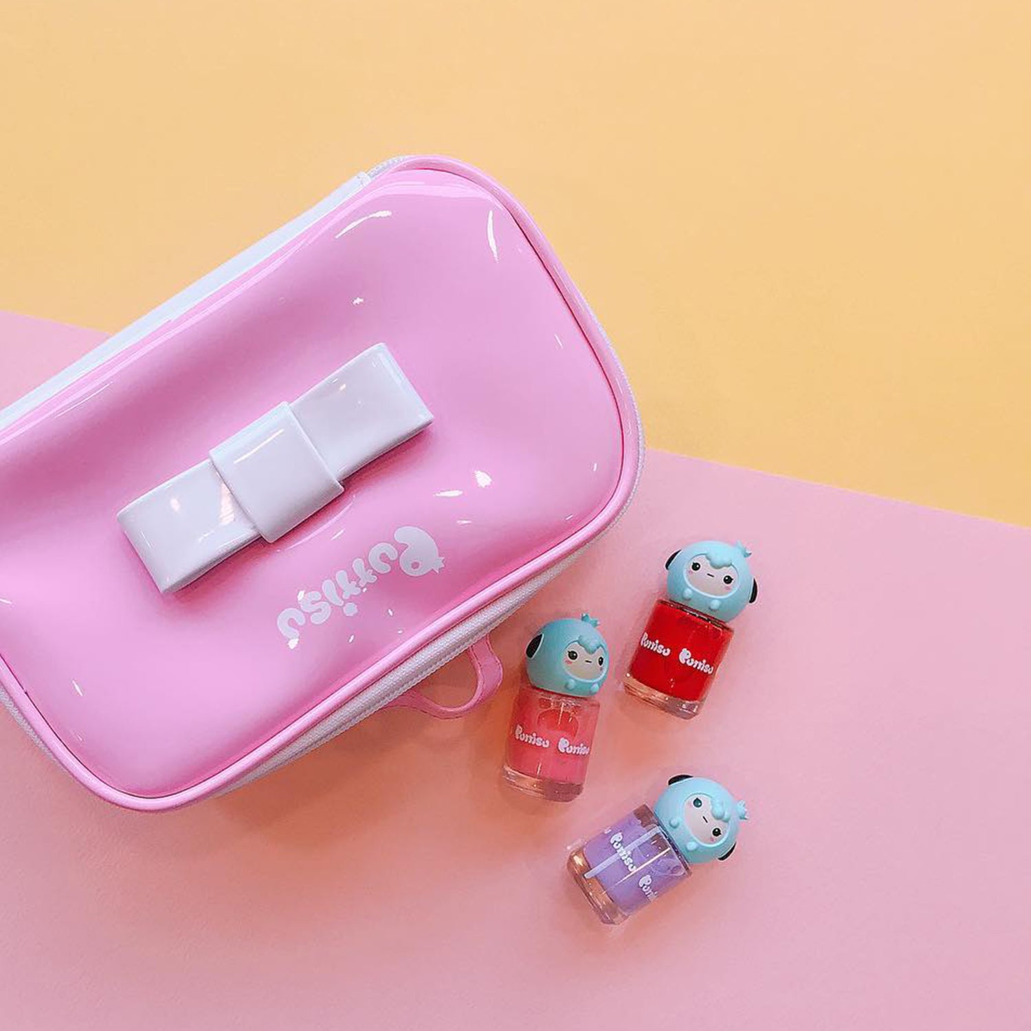 A pink and white pencil case next to three small bottles of cartoon-themed nail polish in red, pink, and purple.