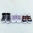 Three pairs of toddler shoe-socks in gray, lavender, and brown, aligned on white fabric.