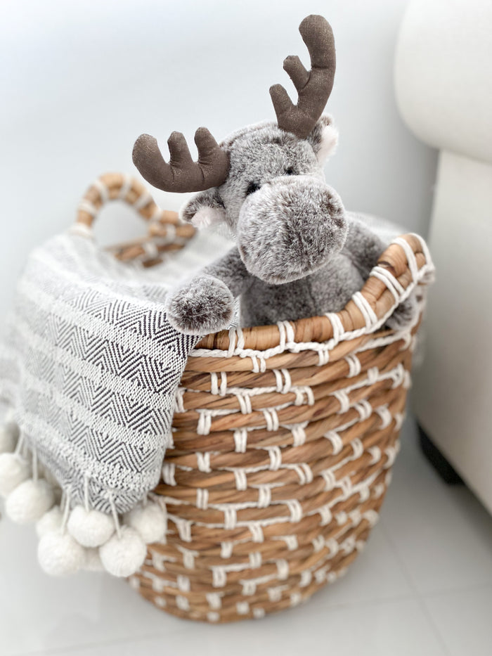 Plush toy reindeer in a woven basket with a blanket on a light background