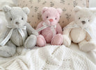 Three teddy bears in gray, pink, and white sitting on a textured surface.