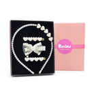 A pearl and white heart hair accessory set displayed in a black presentation box next to a pink gift box. The set includes a pearl headband with white heart accents, three white heart hair clips, and a white bow hair clip with a central white heart.
