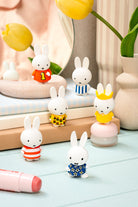 Set of small rabbit figurines in various outfits on a light surface with decorative items in the background.