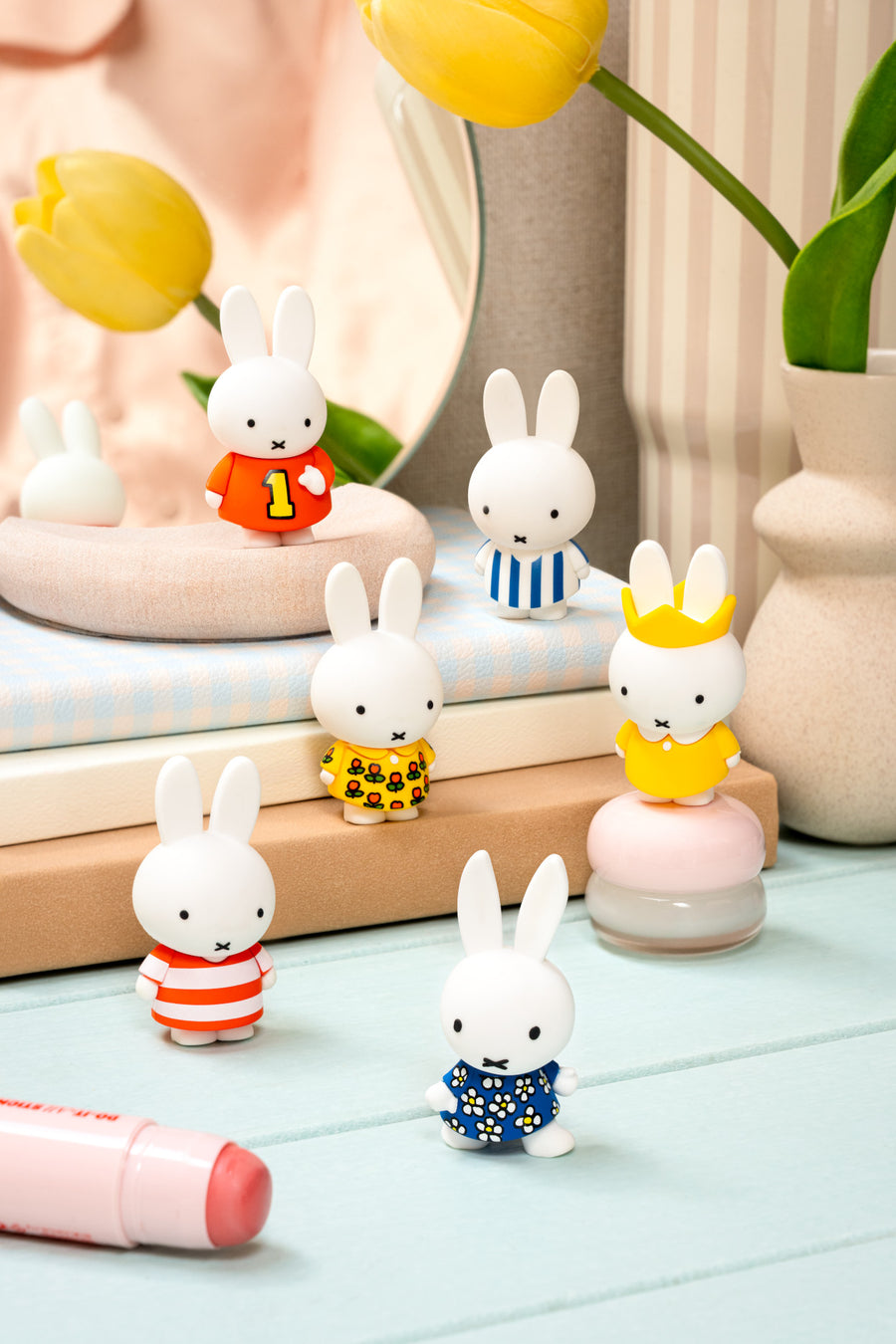 Set of small rabbit figurines in various outfits on a light surface with decorative items in the background.