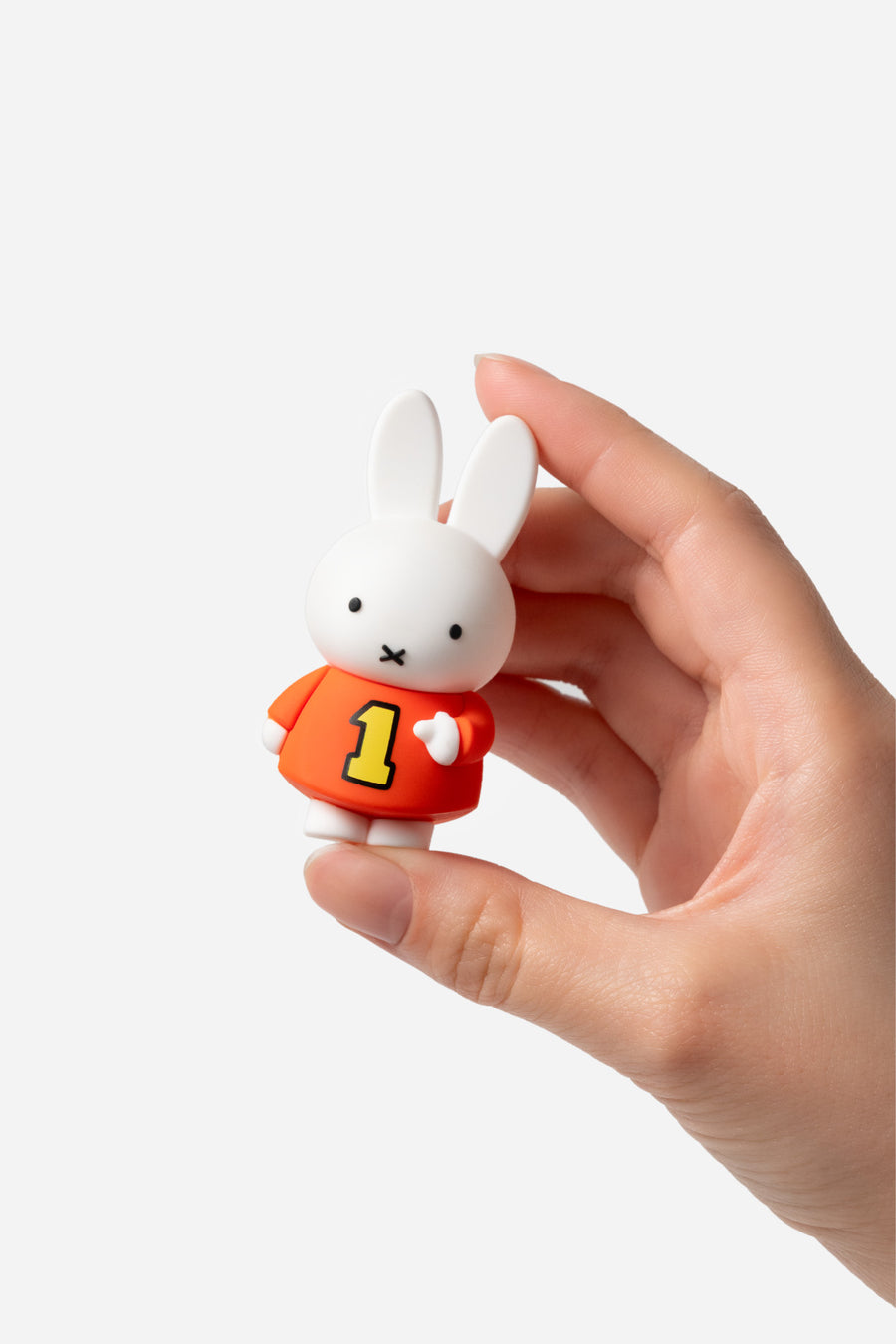 Hand holding a small white rabbit figurine with an orange shirt and yellow number 1 on a white background
