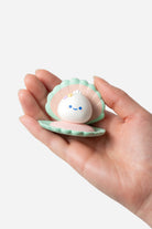 Small white creature with a blue smiley face inside a green shell held in a hand against a white background