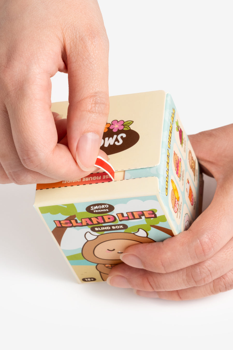 A close-up of hands opening a small illustrated blind box labeled 'Island Life' and 'Smoko'.