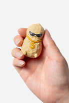 Hand holding a small beige figurine with sunglasses and a yellow tie against a white background