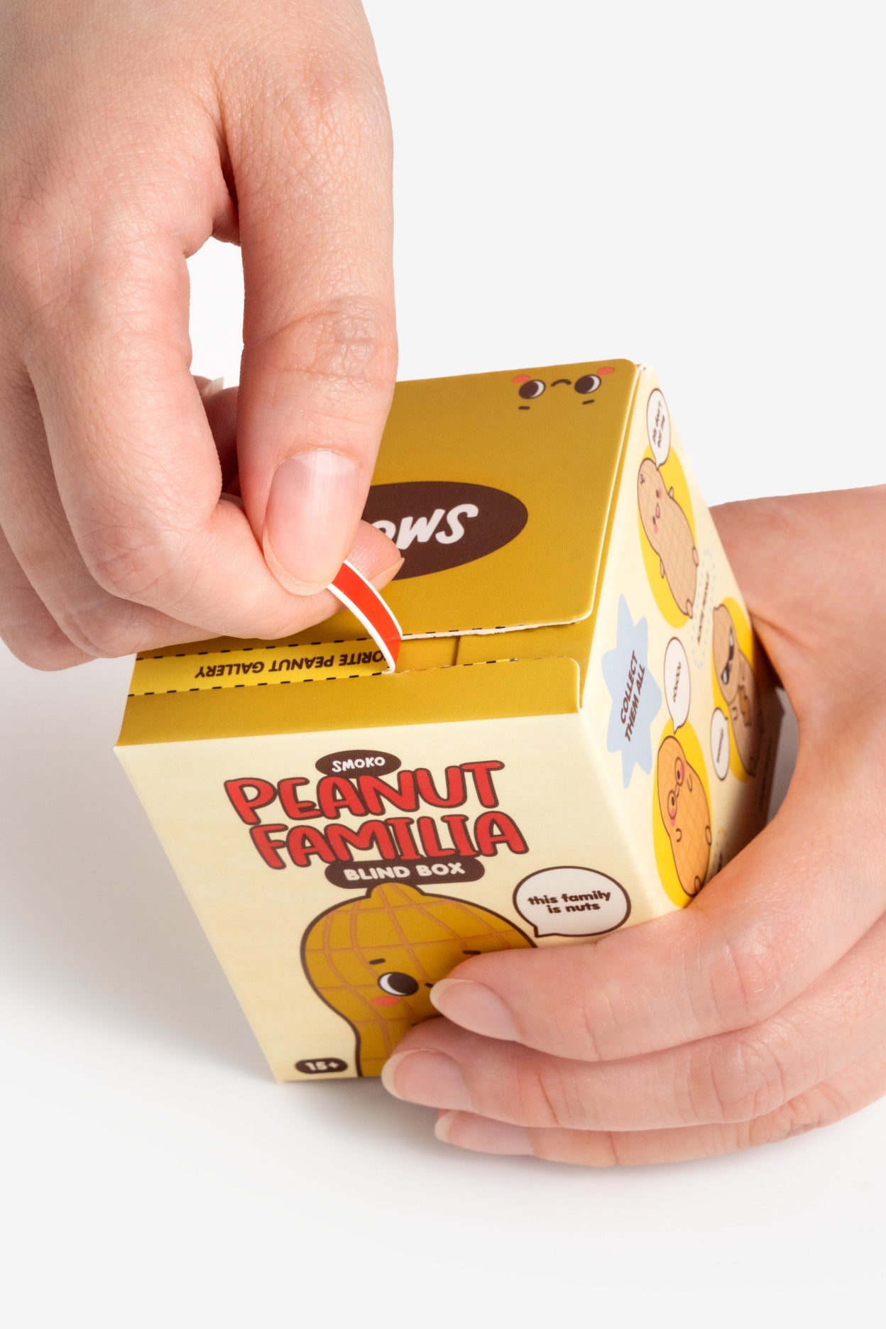 Hand opening a 'Peanut Familia' blind box with a yellow box on a white background