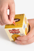 Hand opening a 'Peanut Familia' blind box with a yellow box on a white background