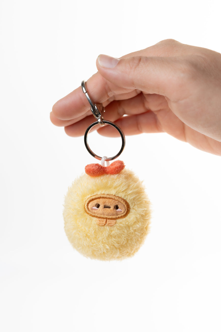 Hand holding a fluffy keychain with a cute face design on a white background