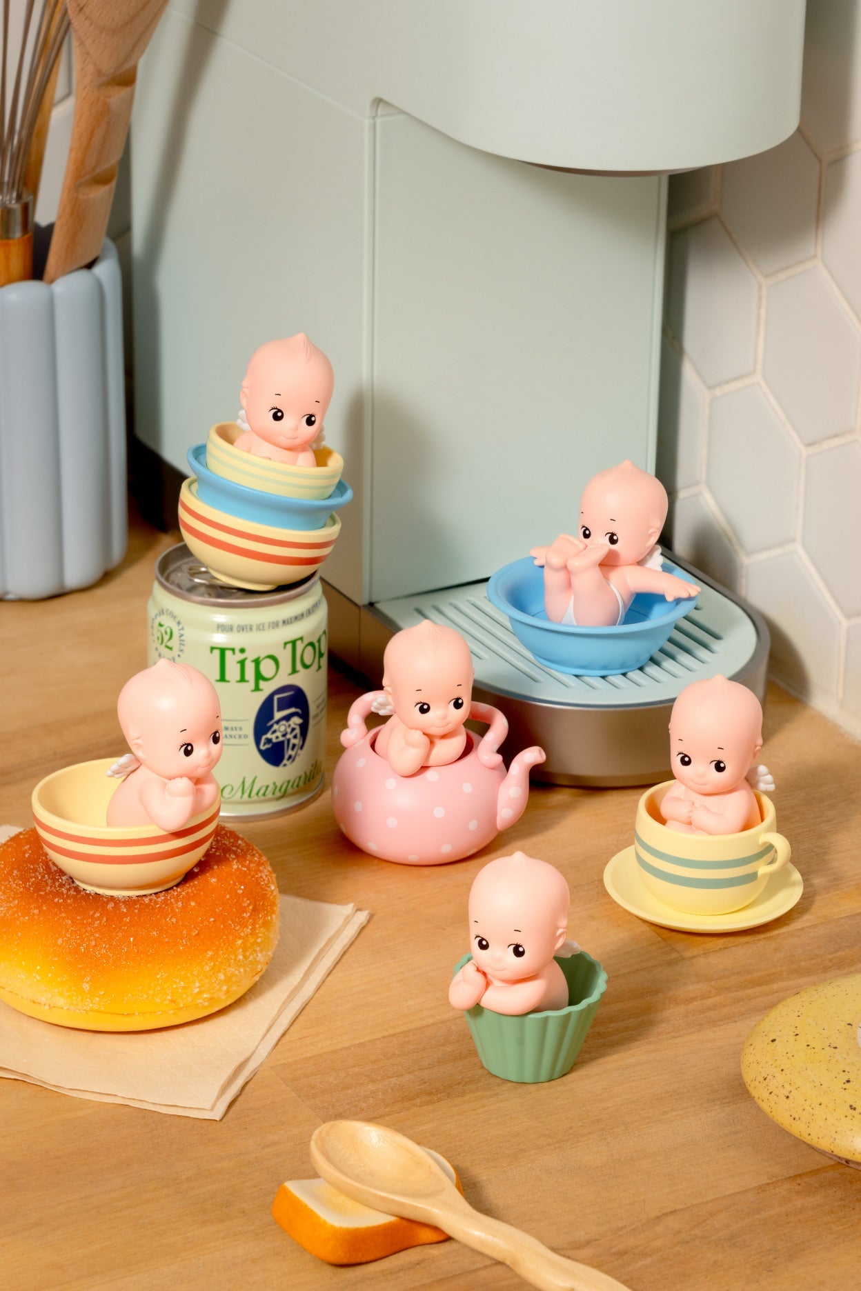 Set of small baby figurines in various kitchen scenarios on a wooden surface.