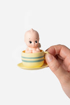 Small figurine of a baby in a yellow cup held by a hand on a white background