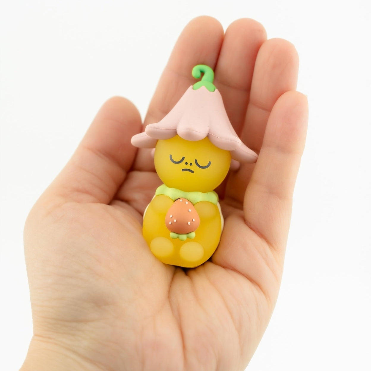 Small yellow figurine with a pink flower on a hand against a white background