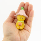 Small yellow figurine with a pink flower on a hand against a white background
