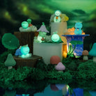 Fairy garden scene with various small figurines and plants against a dark forest background.