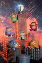 A set of colorful cartoon blob figurines posed on and around stylized gray buildings against a dramatic orange and blue space-themed backdrop with a moon and stars.
