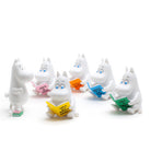 Six white Moomin character figurines arranged on a white background, each holding a brightly colored book in different colors including yellow, pink, orange, blue, green, and teal.
