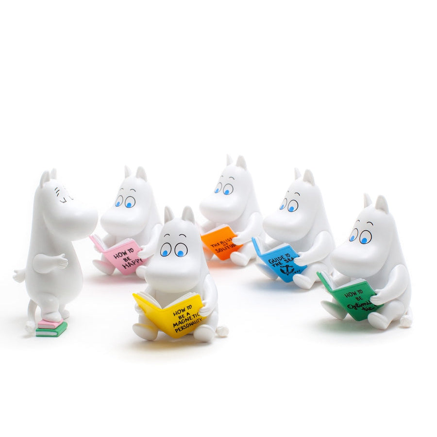 Six white Moomin character figurines arranged on a white background, each holding a brightly colored book in different colors including yellow, pink, orange, blue, green, and teal.