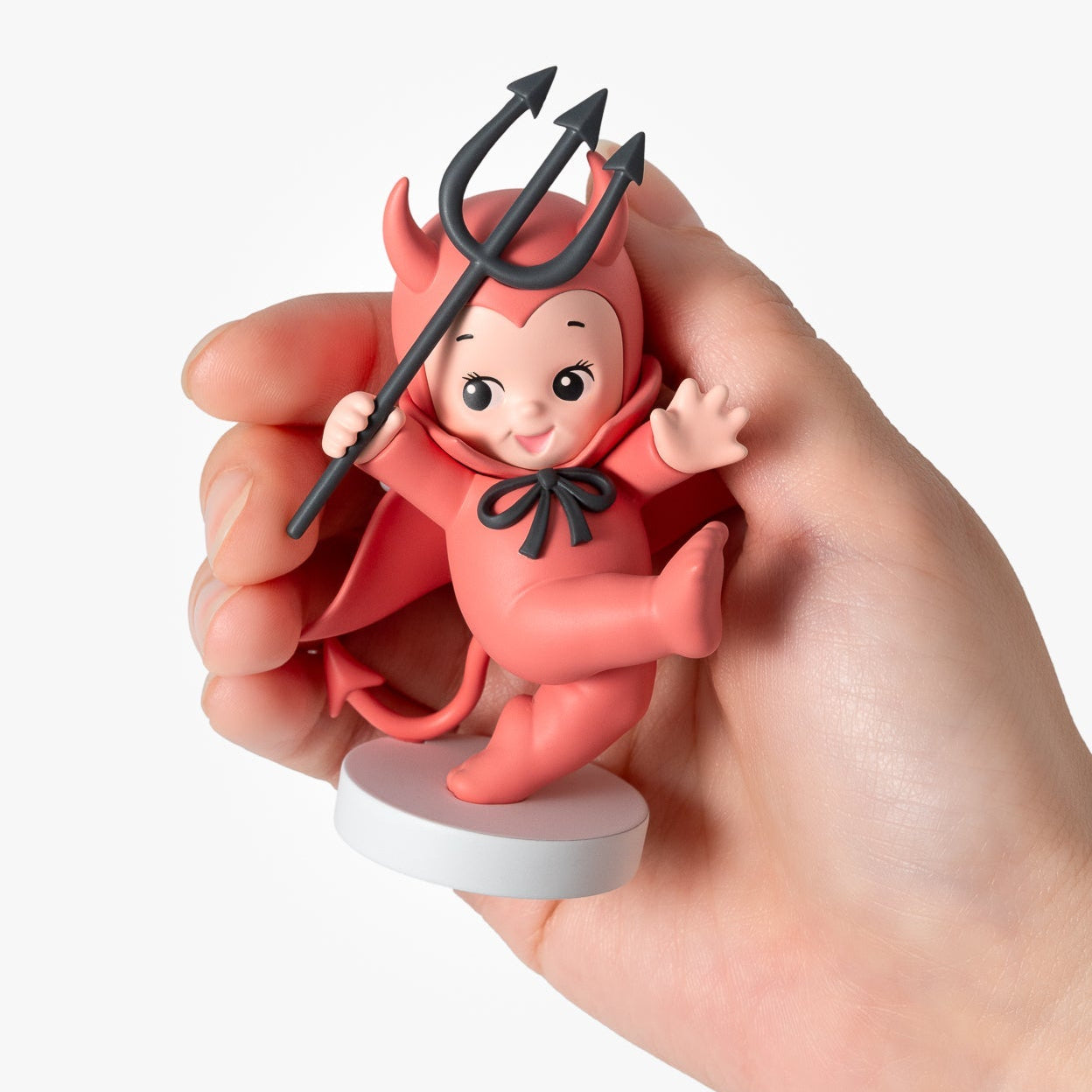 Hand holding a small figurine of a baby with devil horns and a trident on a white background