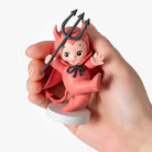 Hand holding a small figurine of a baby with devil horns and a trident on a white background
