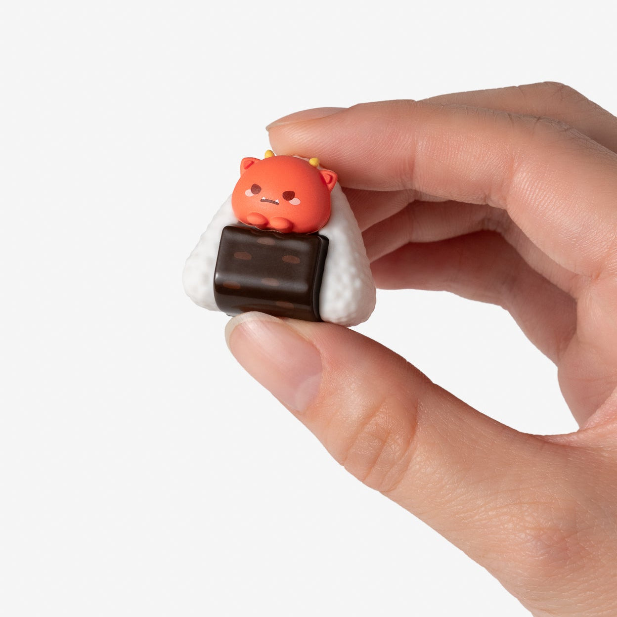 Hand holding a small, cute figurine of a bear inside a rice ball on a white background