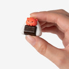 Hand holding a small, cute figurine of a bear inside a rice ball on a white background