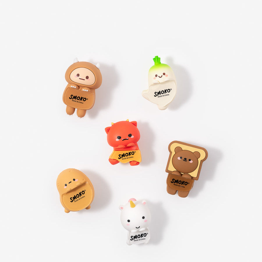 Six small cartoon character charms or pins in assorted colors, including brown, orange, yellow, white, and green, arranged on a plain light background. Each character has the word 'SMOKO' printed on it.