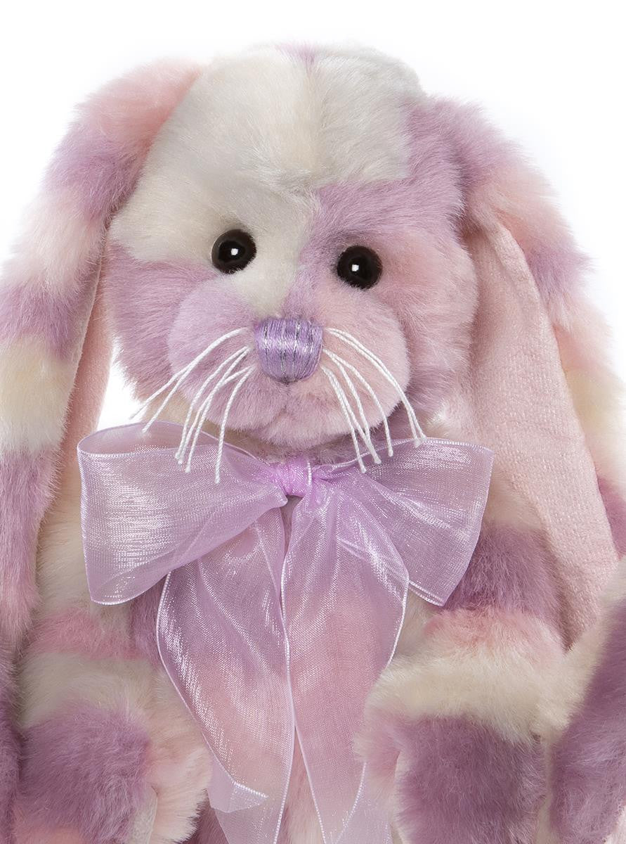 Plush toy rabbit with pink and white fur and a purple bow on a white background