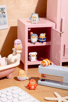 Small figurines in front of a pink locker on a wooden surface