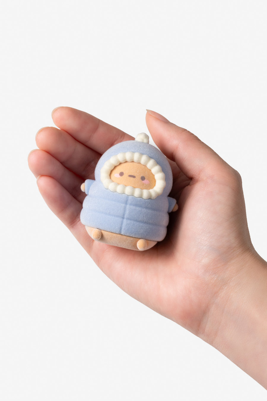 A small plush or soft toy character wrapped in a light blue quilted outfit, held in a person's hand against a plain light background.