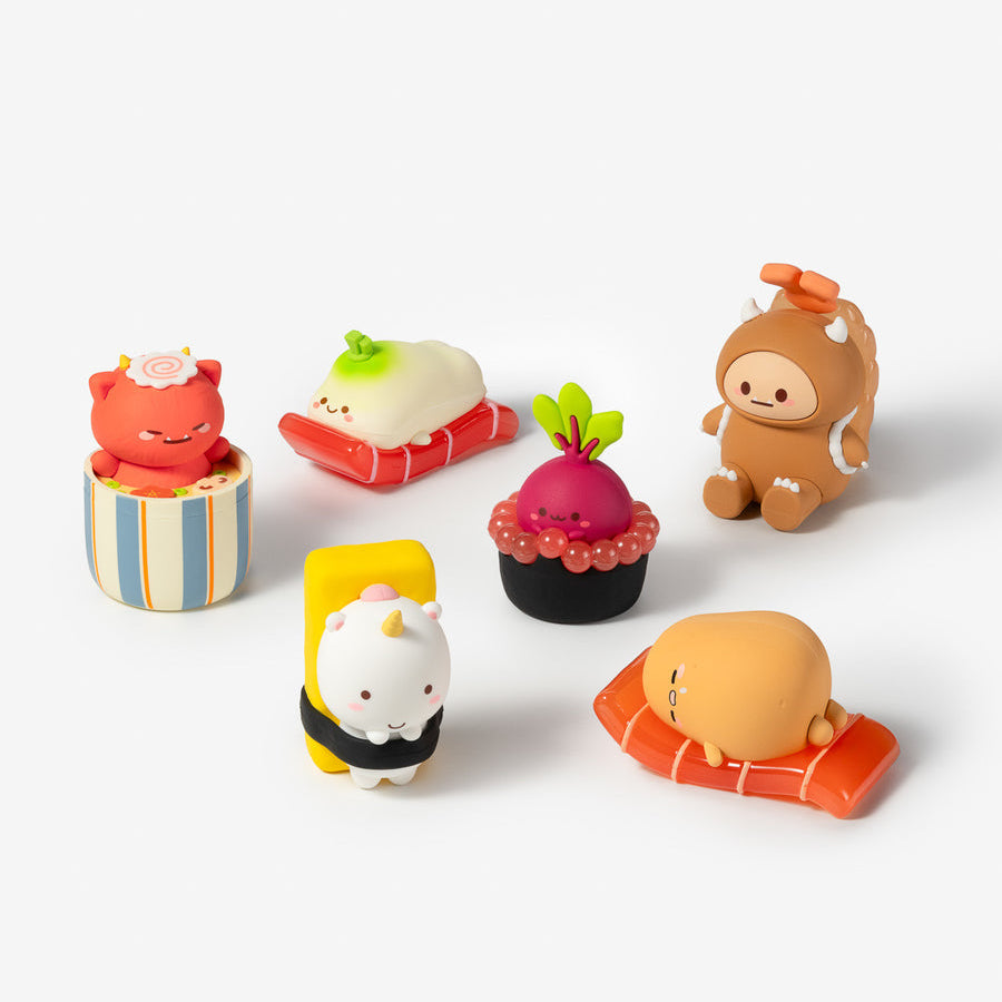 Six small cute character figurines arranged on a clean white studio background. The characters resemble cartoon animals in food-inspired outfits, including sushi, cupcake, and beach towel designs.