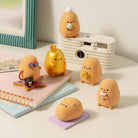 A set of cute, egg-shaped character figurines in various poses and colors, styled on a white table next to a retro camera, notebook, and striped frame.