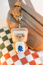 Plush keychain shaped like a sandwich with a face attached to a bag on a checkered surface