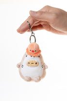 Plush keychain of a cartoon character with a peach-colored hat held by a hand on a white background