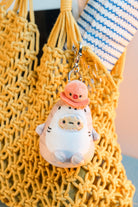 Plush keychain with a peach-colored hat on a yellow textured bag