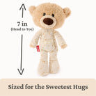 Stuffed teddy bear in pajamas with a measurement label on a white background
