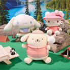 Three plush toys in a scenic outdoor setting with a lake and trees.