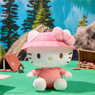 Hello Kitty plush toy wearing a pink raincoat in a forest setting with trees and rocks.