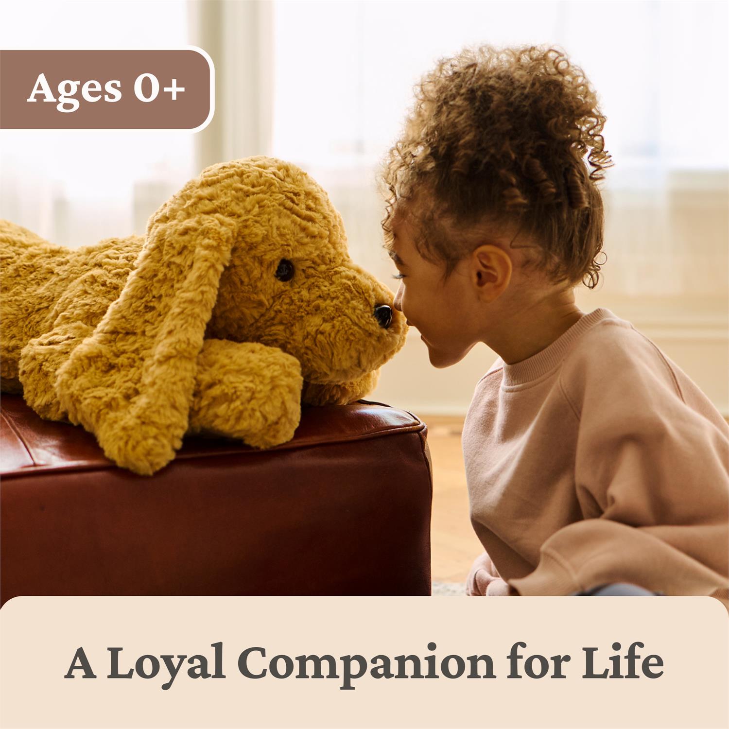 Child playing with a large yellow stuffed animal on a couch, with text indicating age suitability and a tagline.