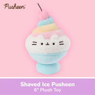 A Pusheen 'Shaved Ice' plush toy shown against a pink background with a purple text banner at the bottom. The plush features Pusheen's face on a white shaved-ice-like top with pastel blue, pink, and yellow stripes, and a light blue base.