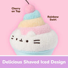 A plush cupcake character toy with a white fuzzy body, pastel pink, yellow, and blue frosting-like layers, a cherry on top, and text labels reading 'Cherry on Top,' 'Rainbow Swirl,' and 'Delicious Shaved Iced Design' on a pink background.