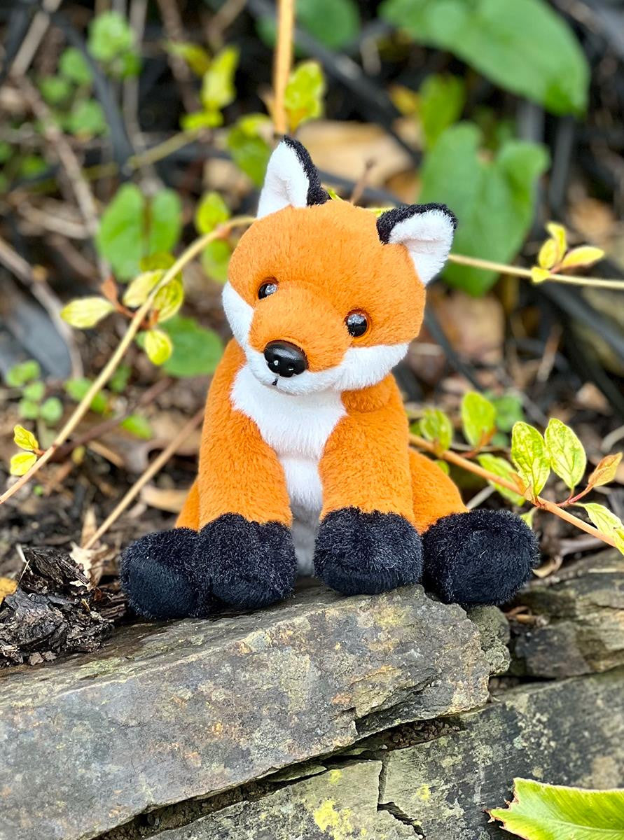 Plush fox toy sitting on a rock with greenery in the background