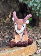 Plush toy goat sitting on a wooden log with a natural background