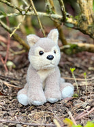 Plush toy wolf sitting on a natural ground with plants in the background